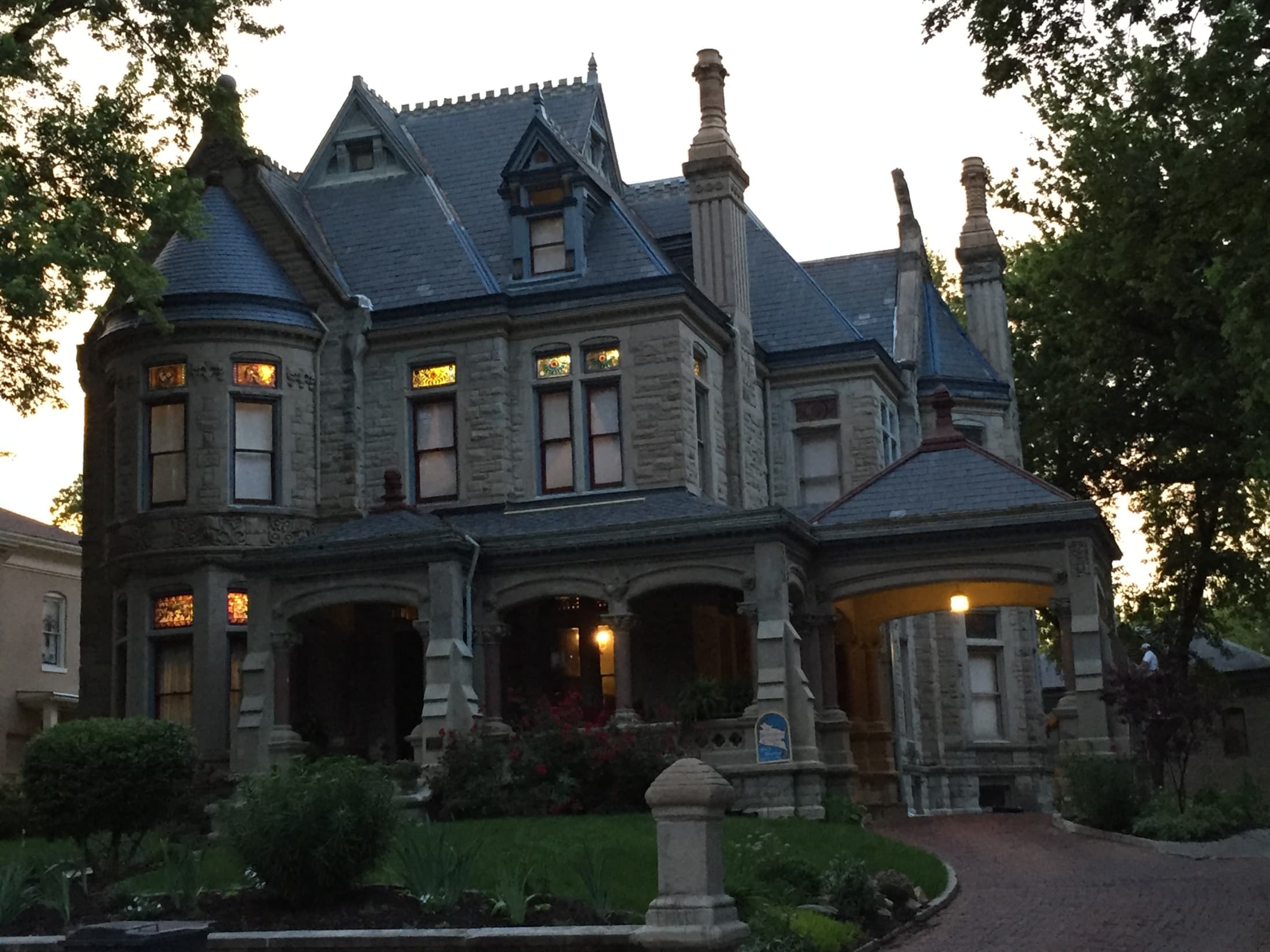 A grand, historic stone mansion with intricate architecture and stained glass windows, set in a landscaped yard.