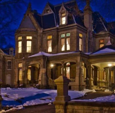 A historic mansion with ornate architecture, illuminated at night and surrounded by snow.