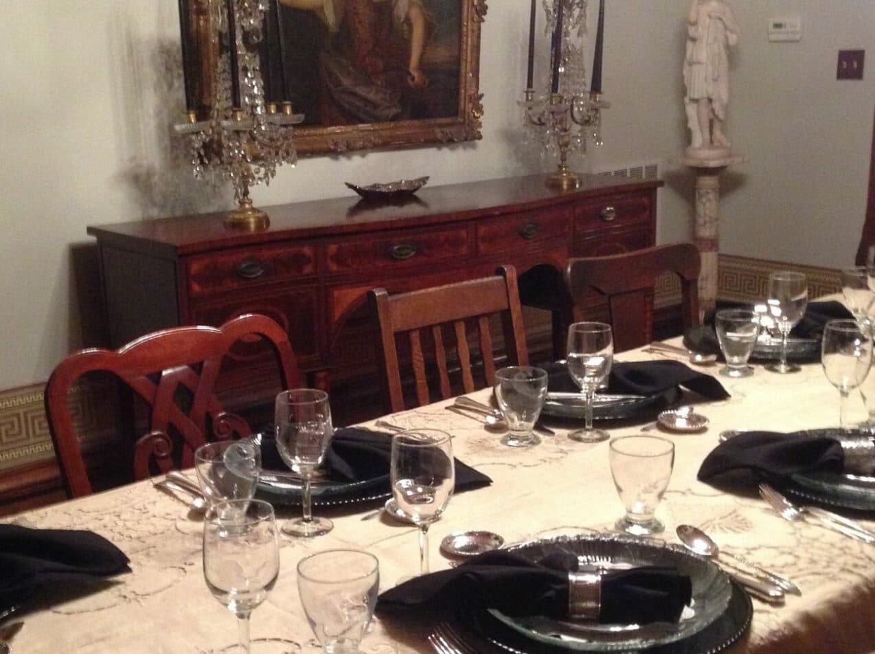 A neatly set dining table with black napkins and glassware, illuminated by ornate candleholders, against an elegant wall decor.