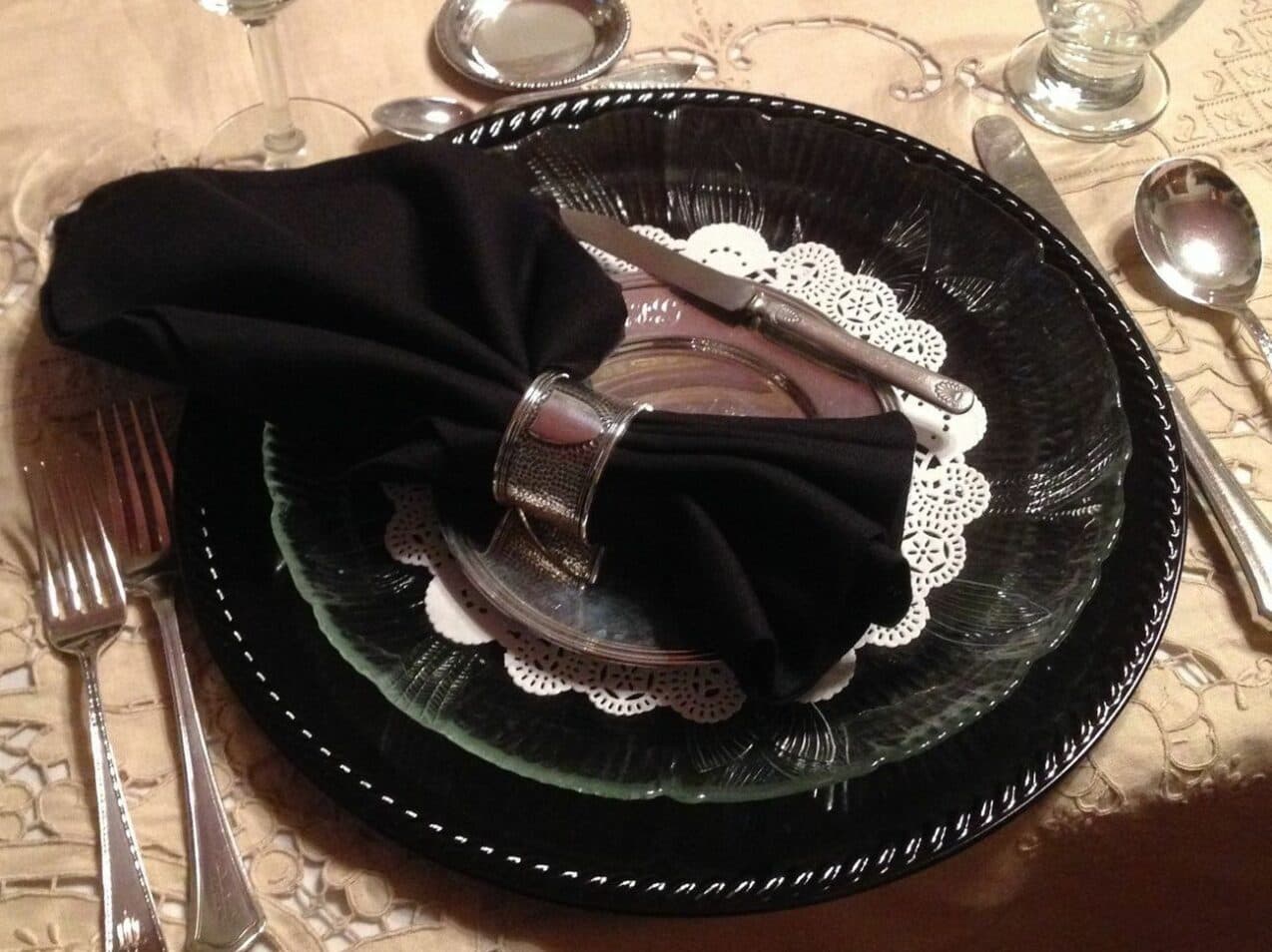 A formal dining setting with a black napkin arranged on a decorative plate.