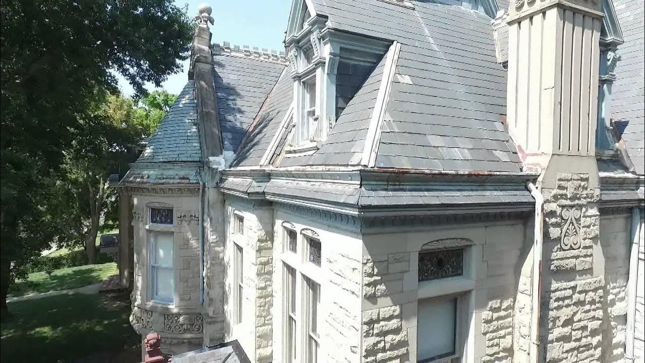 Historic stone building with intricate roof details surrounded by trees.