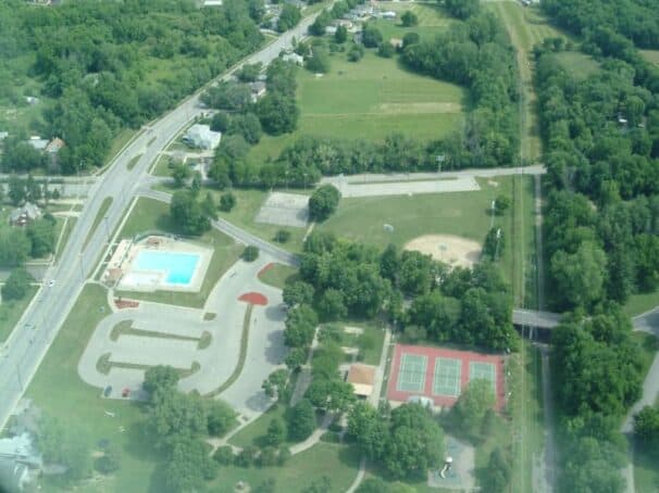 Aerial view of a park featuring a swimming pool, tennis courts, and sports fields surrounded by greenery.