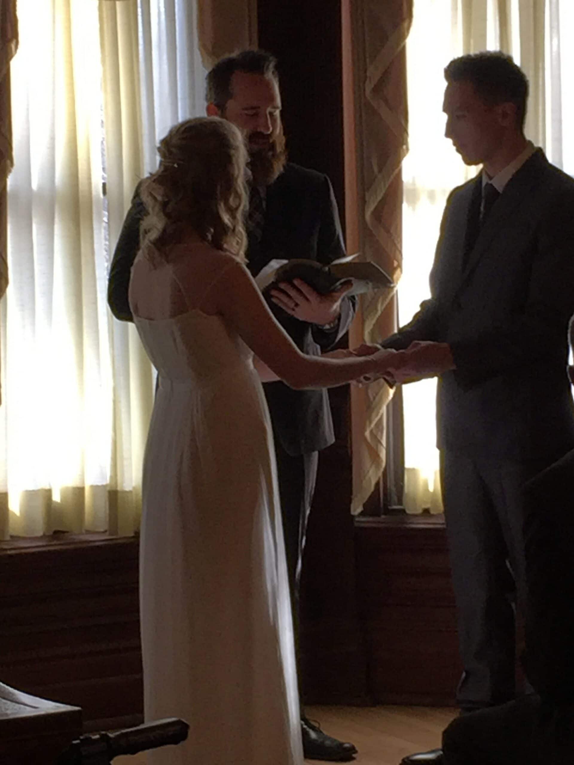 A couple exchanges vows during a wedding ceremony with an officiant holding a book.