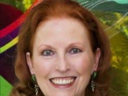 A smiling woman with long red hair and green earrings against a colorful background.