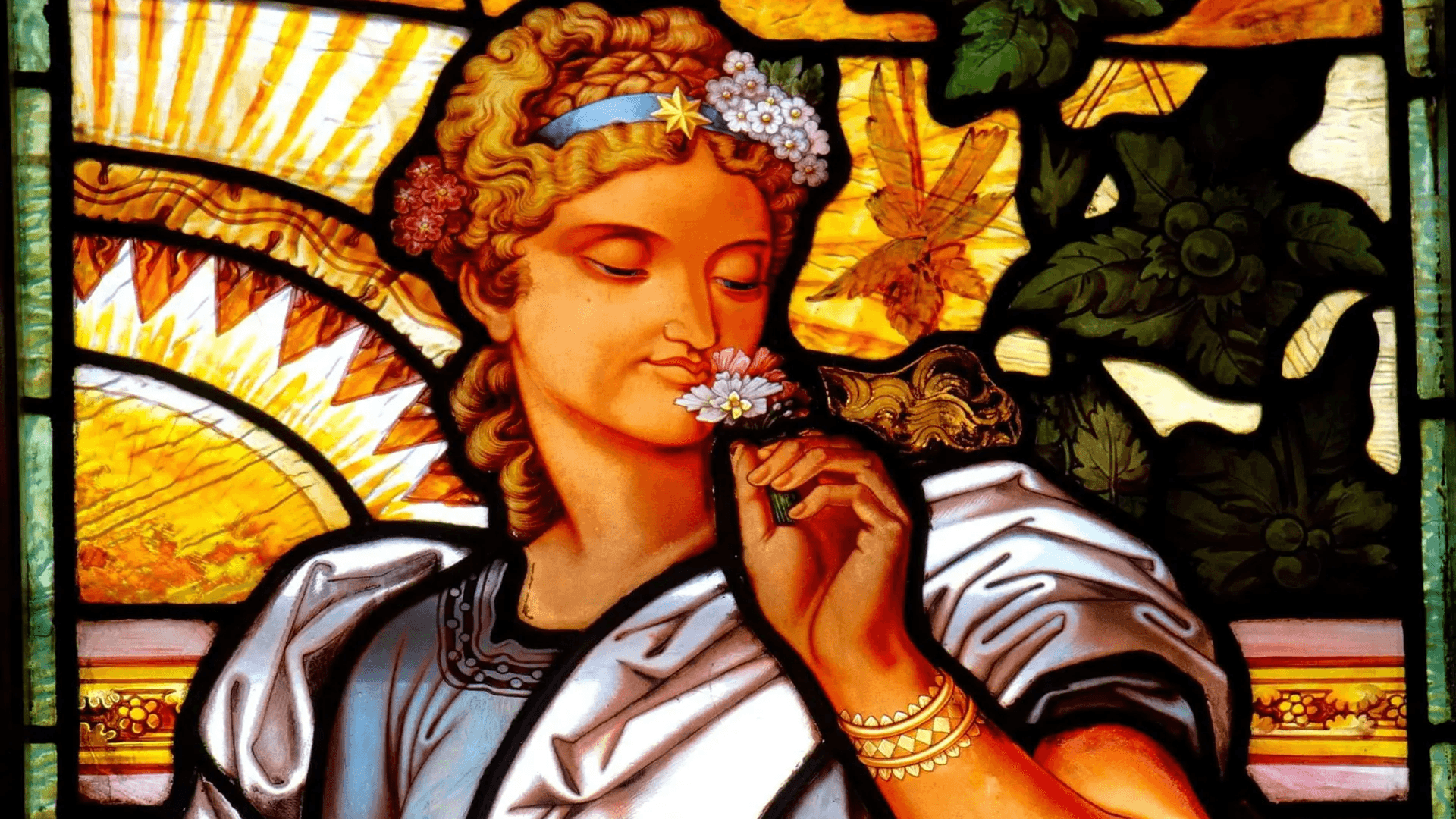A stained glass depiction of a woman gently holding a flower near her face, surrounded by vibrant leaves and abstract patterns.