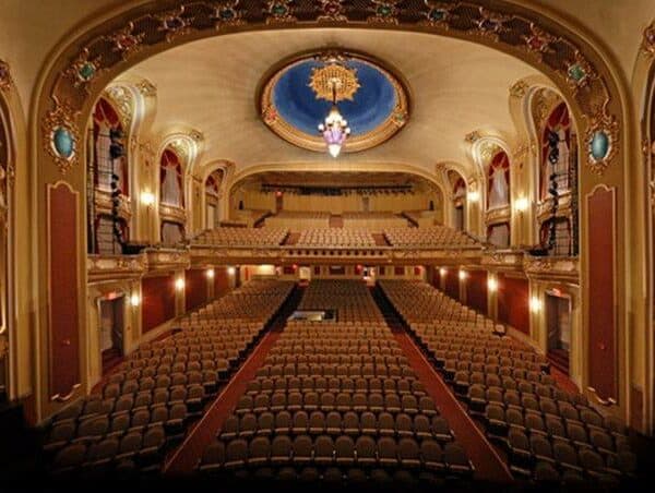 Elegant theater interior with rows of empty seats and an ornate ceiling chandelier.