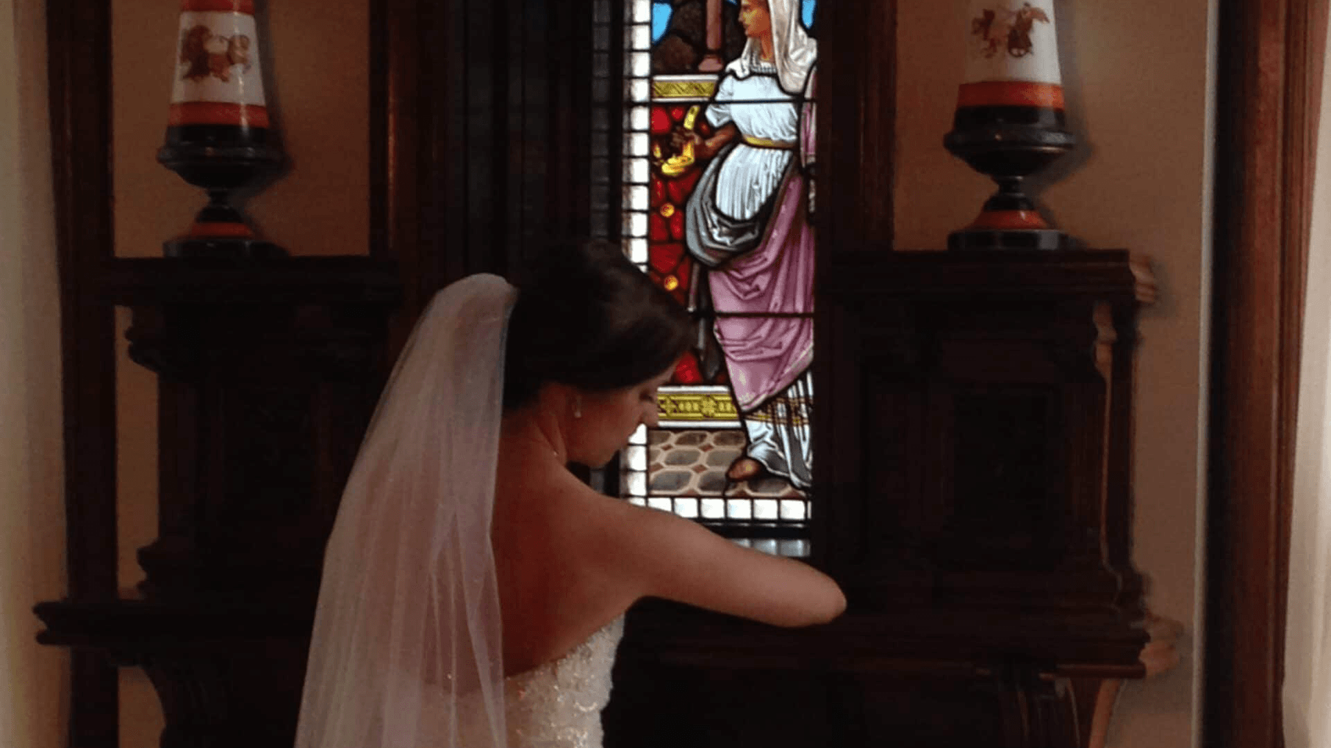 A bride is adjusting her dress in front of a stained glass window.