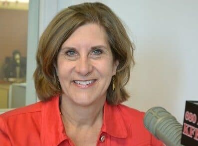 A smiling woman in a red jacket sits in a radio studio.