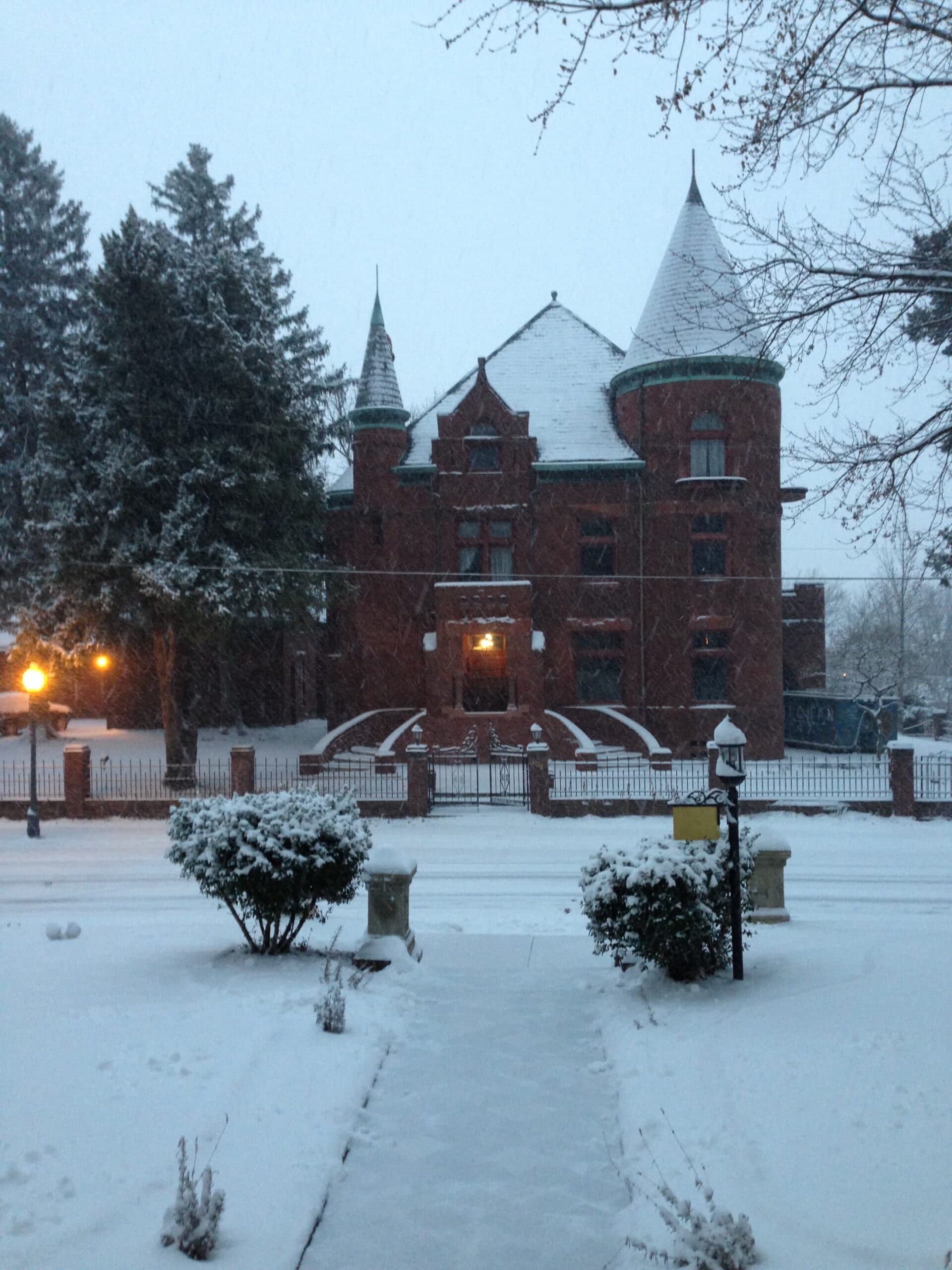 A snow-covered historic building is illuminated by streetlights on a winter evening.