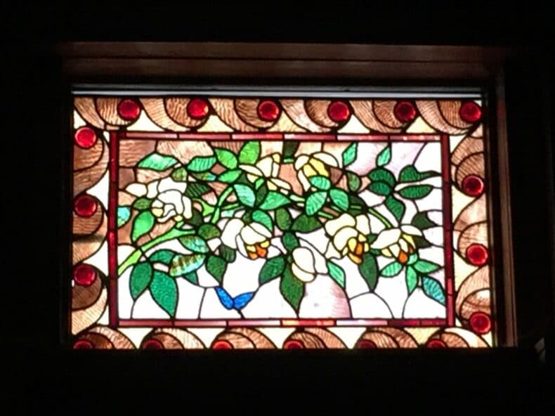 Stained glass window featuring white flowers, green leaves, and a blue butterfly.