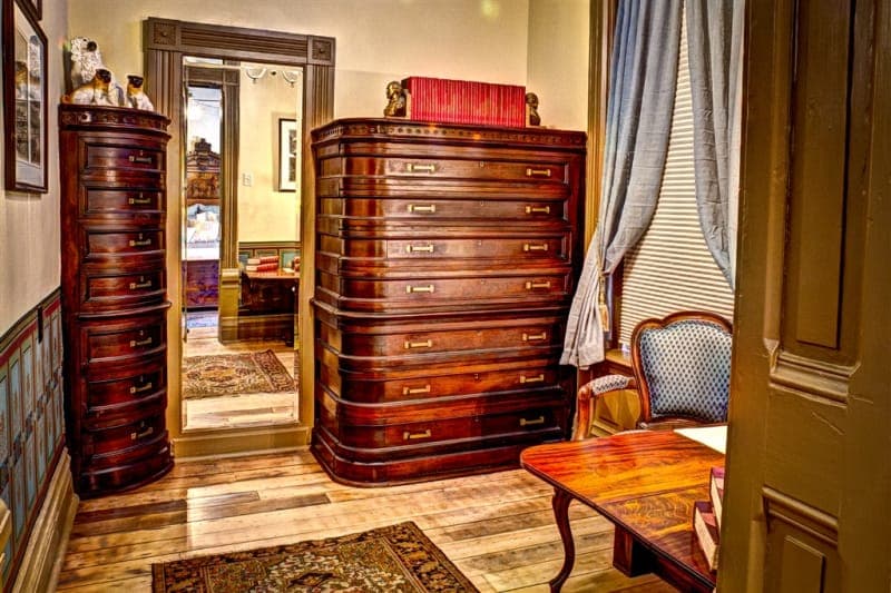 A vintage-style room featuring ornate wooden dressers, a mirror, and a cozy seating area.
