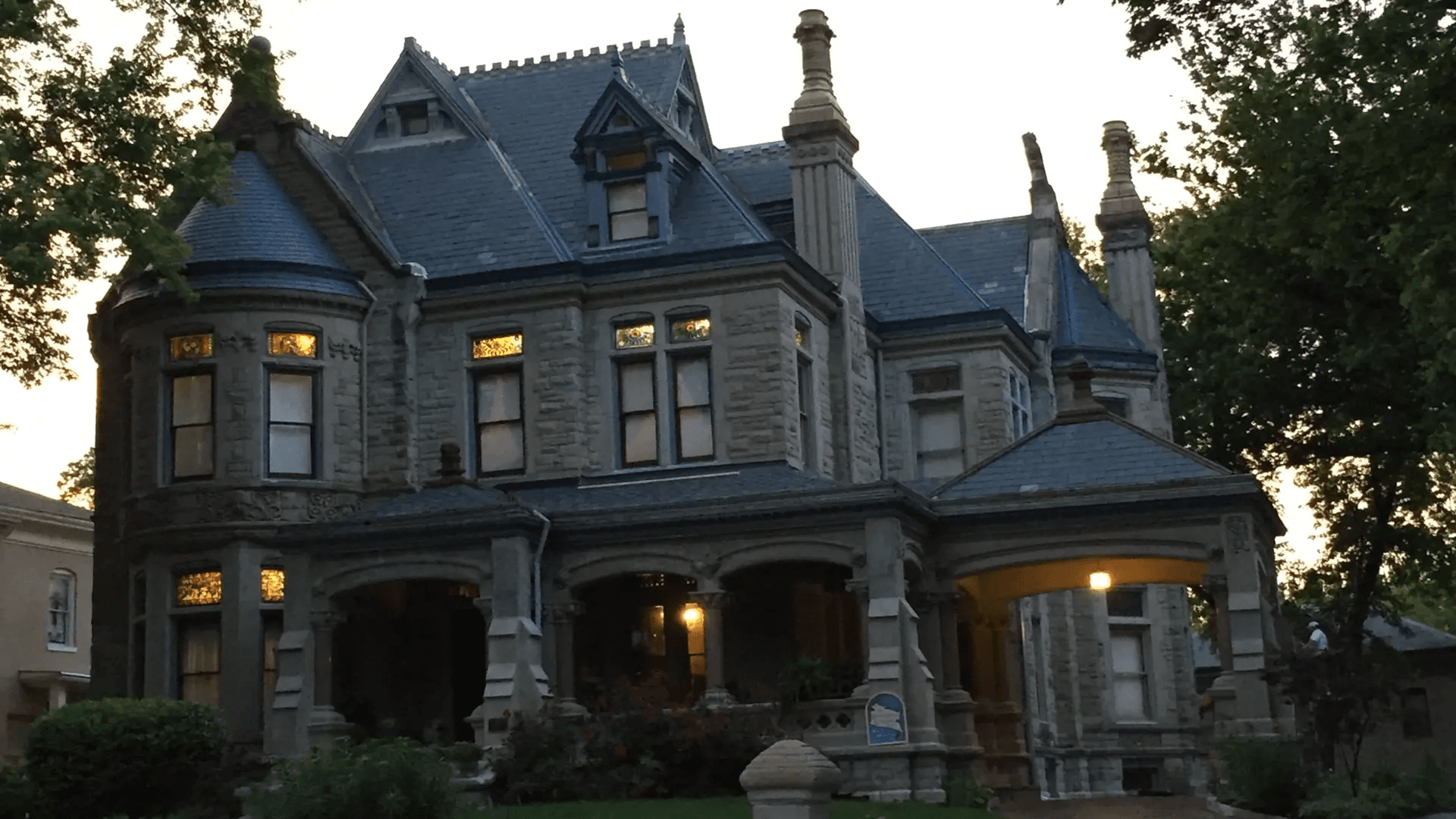 A large, ornate stone mansion with a blue slate roof and decorative details, illuminated at dusk.