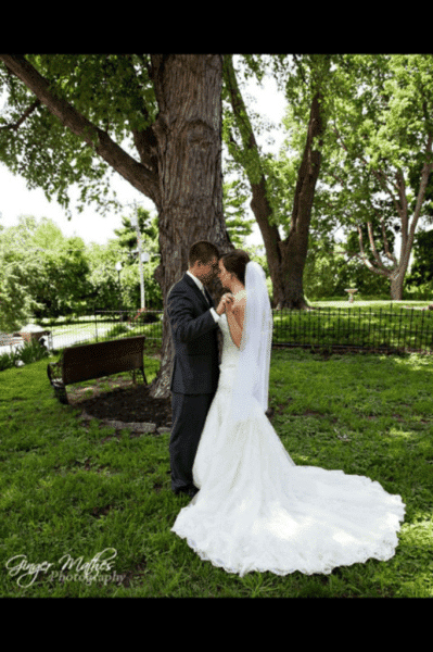 A bride and groom share a tender moment under a tree in a lush green park.