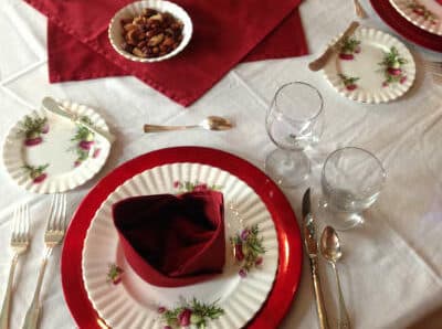 A beautifully set dining table featuring floral plates, red accents, and glassware.