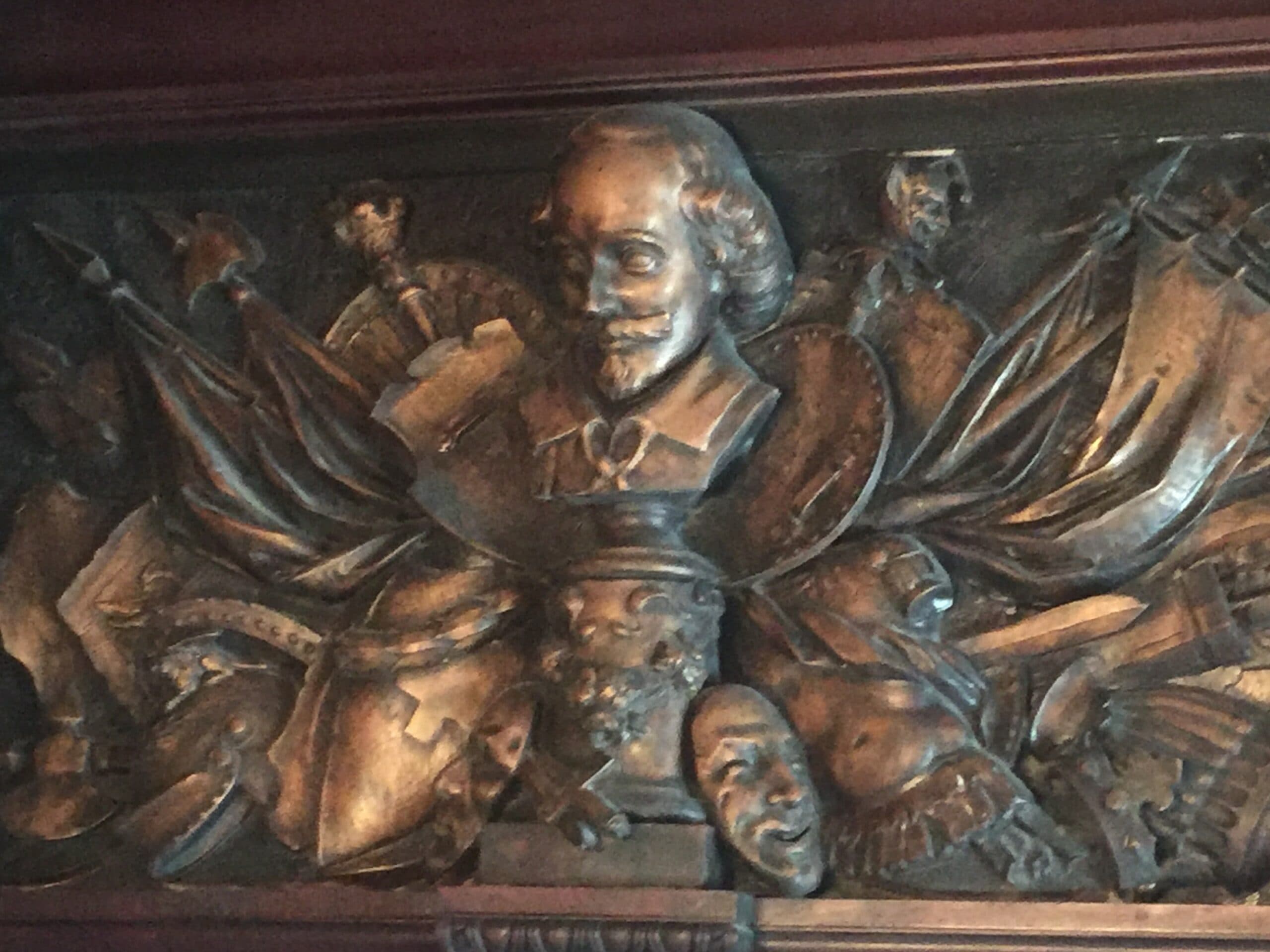 A detailed bronze relief featuring a bust of a man among various historical symbols and faces.