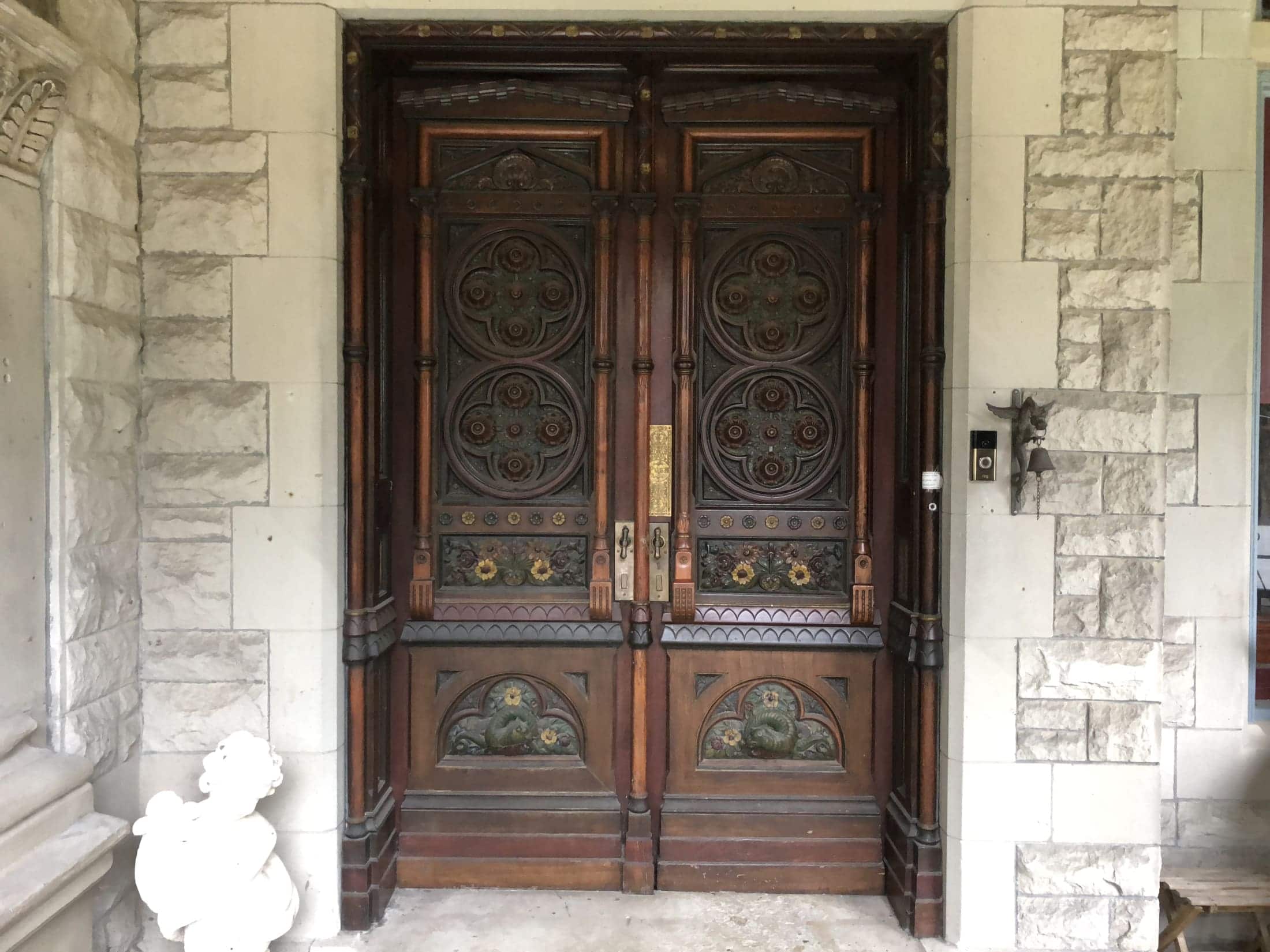 Elaborately carved wooden double doors framed by stone walls and a decorative statue.
