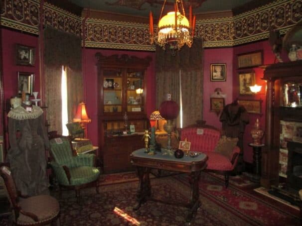 A cozy, vintage parlor featuring rich purple walls, ornate furniture, and eclectic decor.