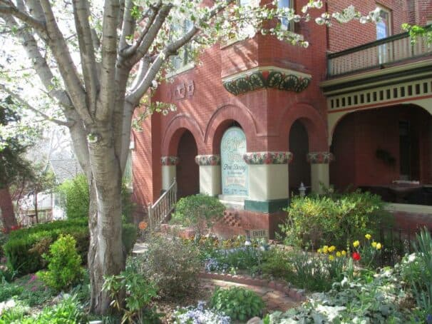 A charming brick house with arched windows surrounded by blooming gardens and a tree.