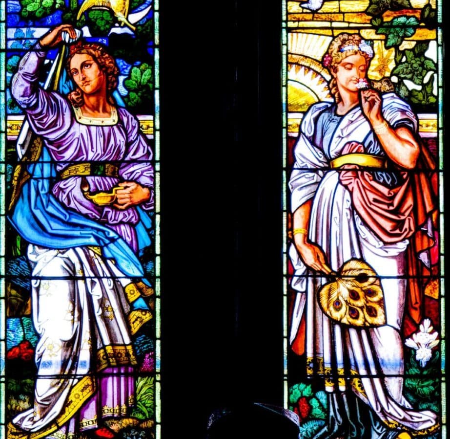 Stained glass window featuring two elegantly dressed figures, one holding a lamp and the other a fan.