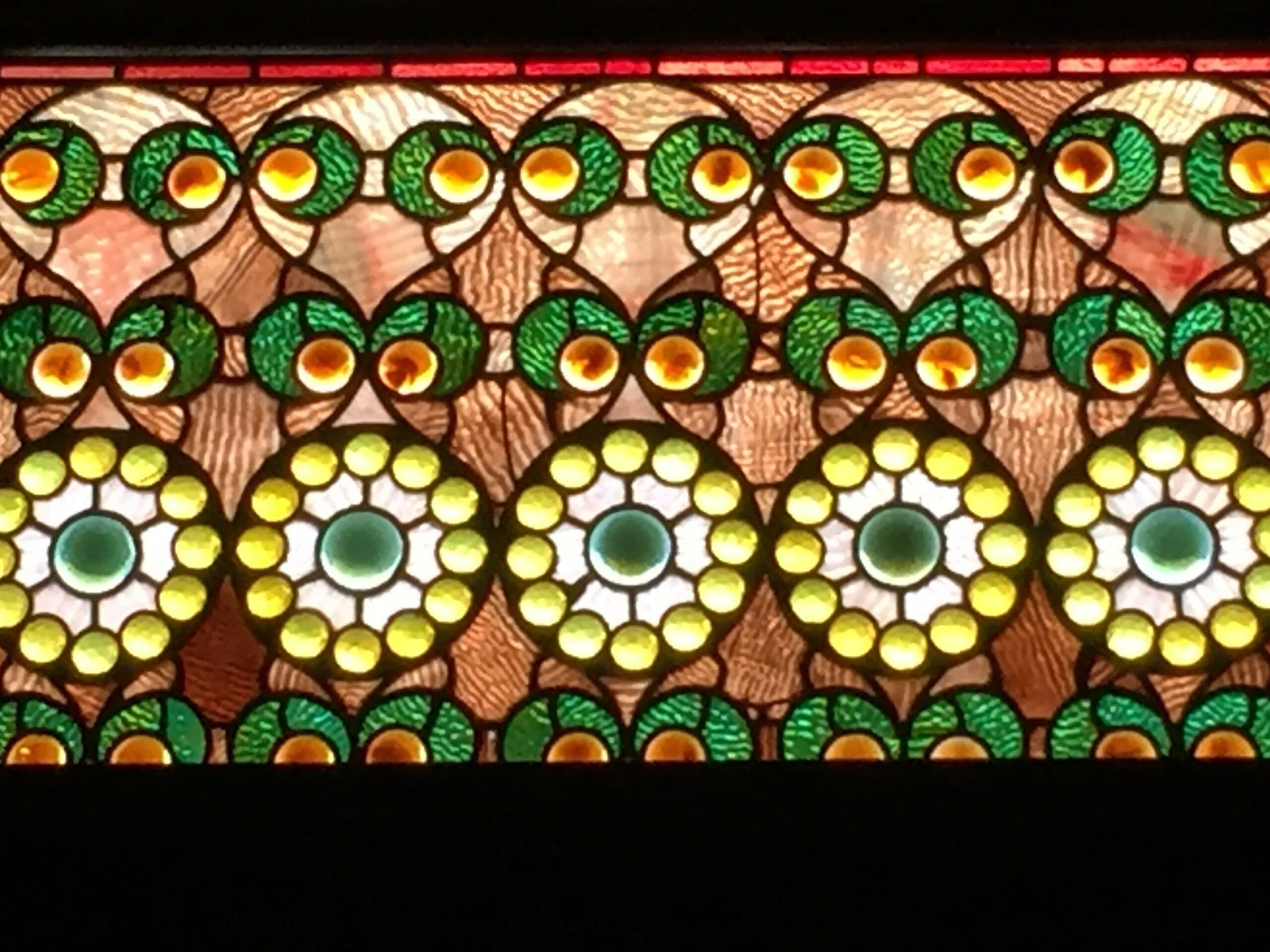 Colorful stained glass featuring circular and floral patterns in green, yellow, and brown tones.