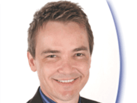 A smiling man in a suit with short hair against a light background.
