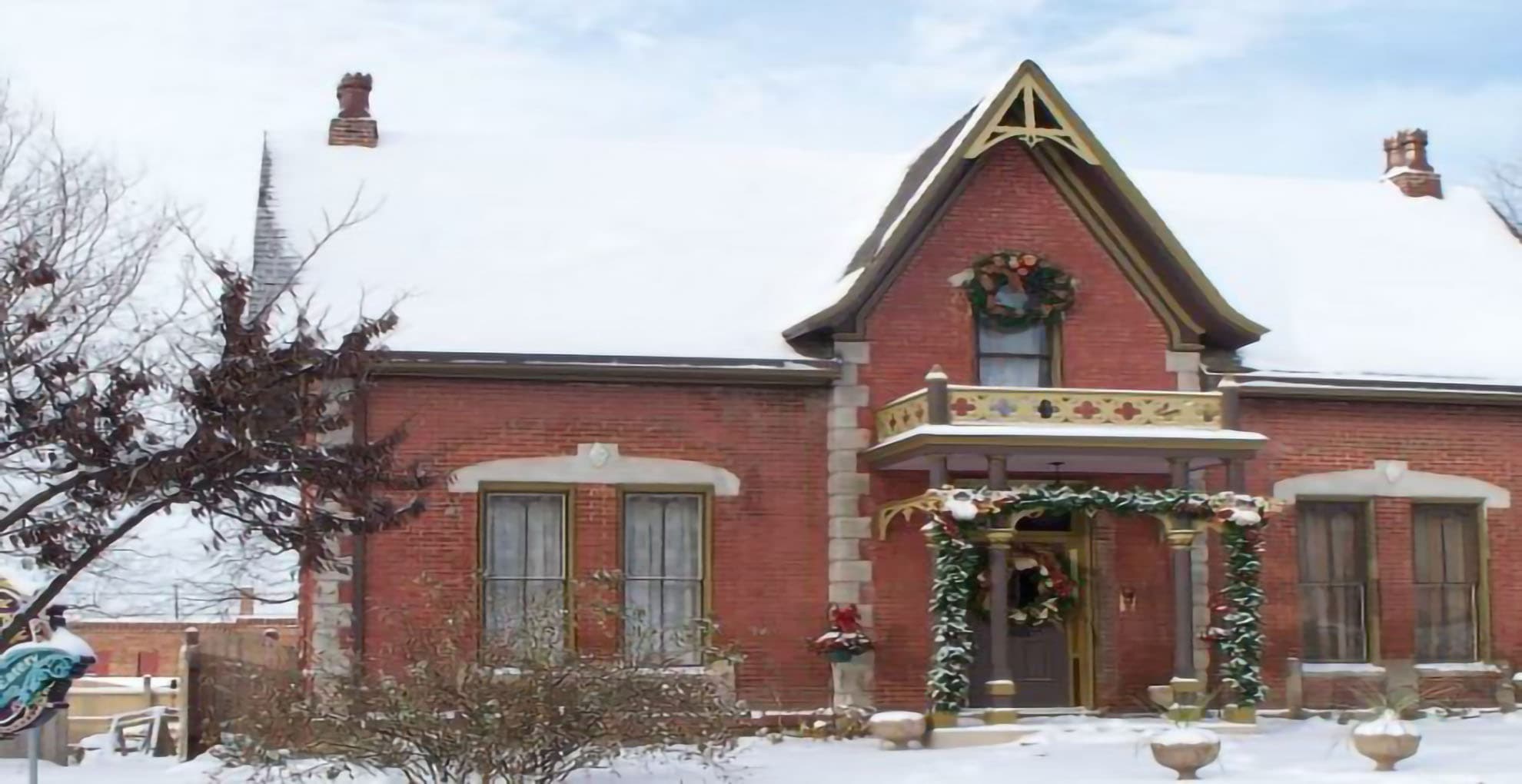 A charming red brick house adorned with holiday decorations in a snowy landscape.
