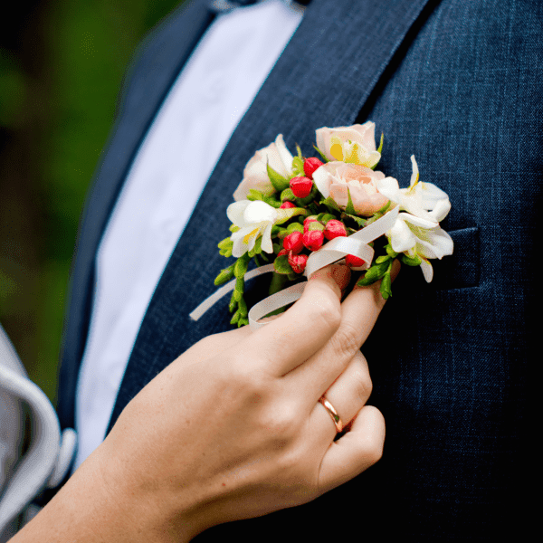 A hand adjusts a floral boutonniere on a man's suit jacket.